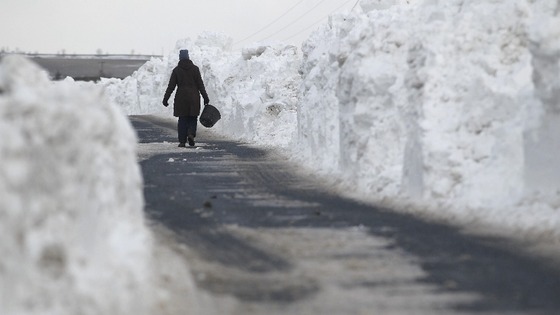 A farmhand makes her way through a wall of snow piled up along a road in the Briercliffe area of Burnley