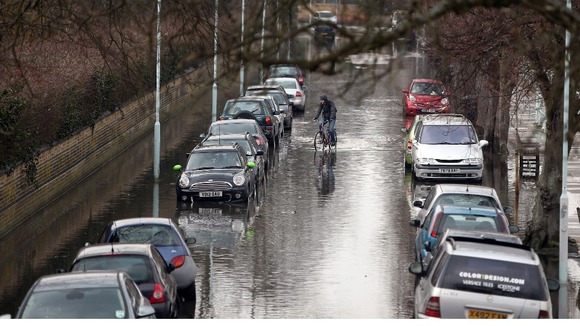 A cyclist rides down Ranelagh Drive in Richmond which was briefly flooded due to spring tides leaving parked cars under water