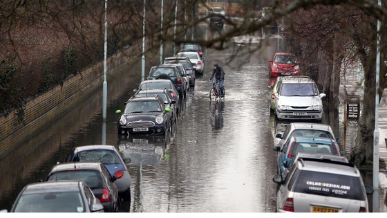 A cyclist rides down Ranelagh Drive in Richmond which was briefly flooded due to spring tides leaving parked cars under water