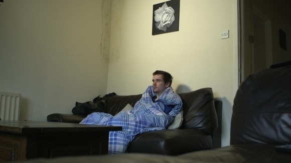Man sits on sofa wrapped in blanket