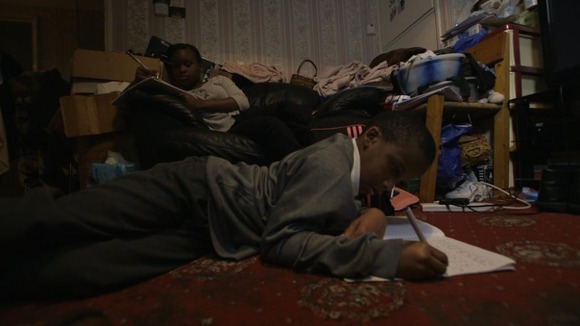 Young boy does homework on floor in crowded room