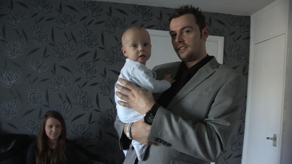 Man holds baby with mother in background