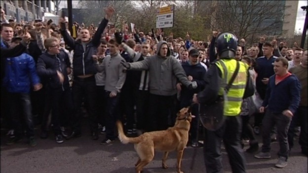 Fans chant as the police keep them back.