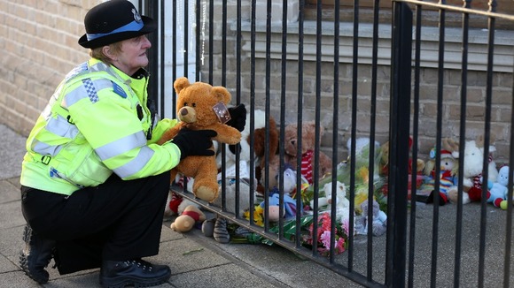 A PCSO lays a tribute from a member of the public outside the flat where the three children were found