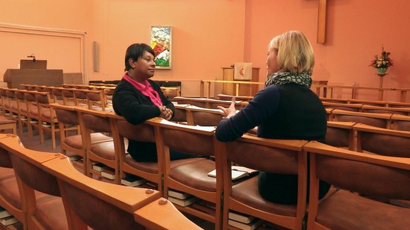 Two ladies sit on chairs in a church chatting