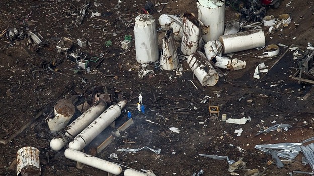 Investigators stand amid the aftermath of the massive explosion