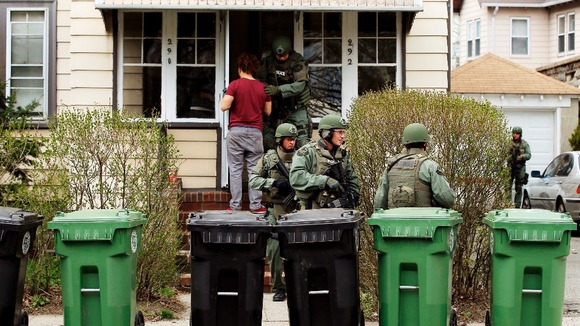 A resident watches as police officers search houses for Dzhokhar Tsarnaev.