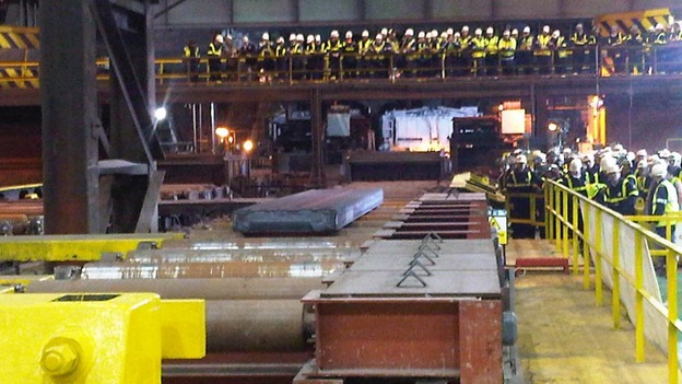 Workers look on as the first piece of steel is produced