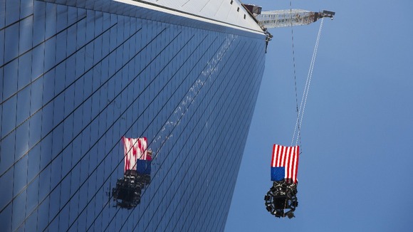US flag flutters in the wind as the final piece of a spire is lifted above New York