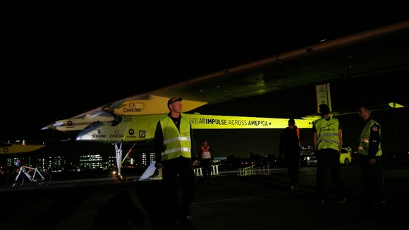 Solar Impulse crew members stand next to their sun-powered aircraft on the runway before take-off