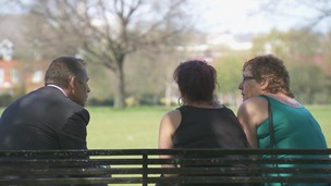 Man on park bench chats to 2 women seen from behind
