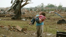 A woman carries a child through a field near the collapsed Plaza Towers Elementary School in Moore, Oklahoma