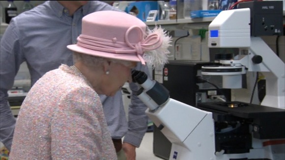 Queen looks down a microscope