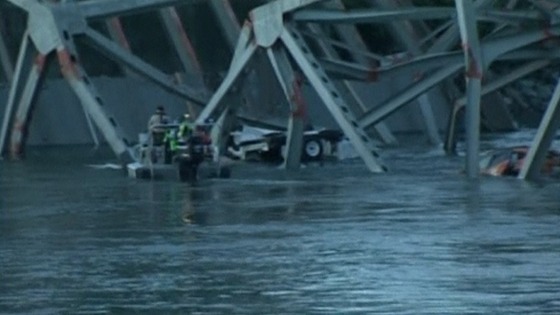 Rescue workers examine two cars submerged in water after the bridge collapse.