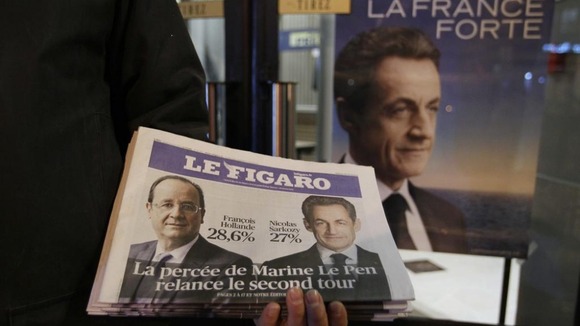 A newspaper seller displays an early edition of Le Figaro
