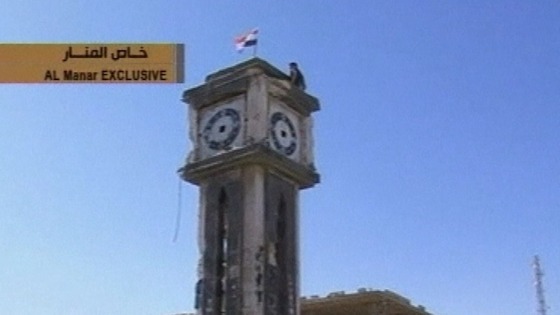 A soldier plants a Syrian flag atop a clock tower in the western town of Qusair