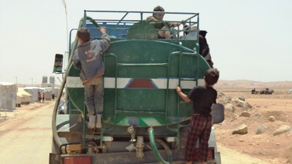 Children hitch a ride on a water truck in the Zaatari refugee camp