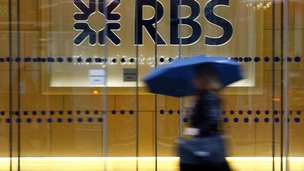 A woman walks past the headquarters of the Royal Bank of Scotland in the City of London with an umbrella.