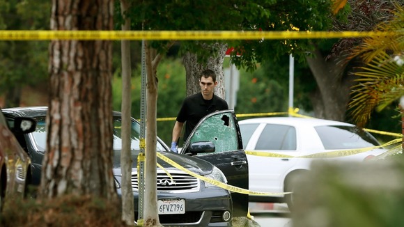 A police officer is seen by a bullet riddled car