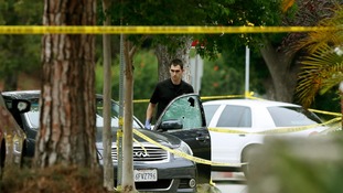 A police officer is seen by a bullet riddled car
