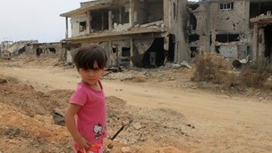 A child in front of a damaged house in Qusair 