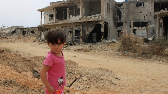 A child in front of a damaged house in Qusair