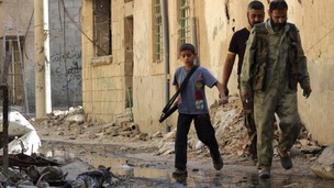 A boy carries a weapon as he walks with members of the Free Syrian Army in Deir al-Zor