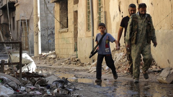 A boy carries a weapon as he walks with members of the Free Syrian Army in Deir al-Zor