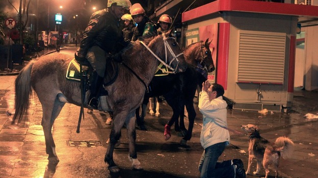 A woman kneels in front of mounted riot policemen amid anti-government protest in Porto Alegre, southern Brazil