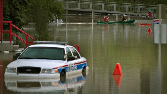 Residents pass a submerged police car by canoe in the city of Calgary
