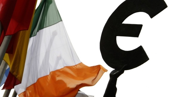 An Irish flag flies next to a symbol of the euro currency at the entrance of the European Parliament in Brussels.