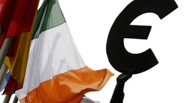 An Irish flag flies next to a symbol of the euro currency at the entrance of the European Parliament in Brussels.