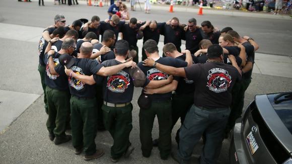Firefighters pray in front of a memorial dedicated to the 19 firefighters
