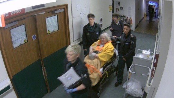Old lady on bed-trolley in corridor pushed by paramedics
