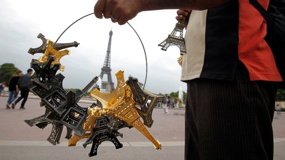  souvenir vendor sells Eiffel tower models for tourists in front of the Eiffel Tower.