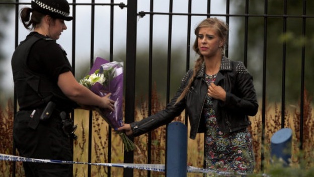 A well-wisher hands over some flowers to a police officer at the scene of a stabbing in Moston, Manchester.