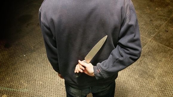 A general view of a man in a hoodie holding a knife