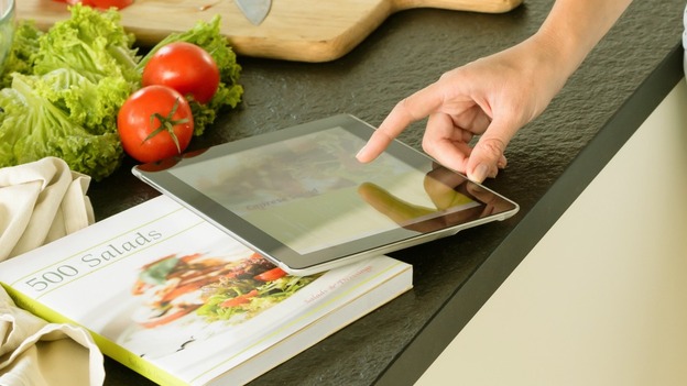 Woman using tablet recipe book searching kitchen wine vegetables.
