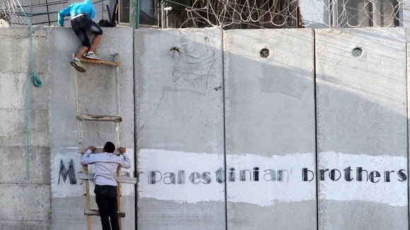 Two Palestinians climb over the security barrier