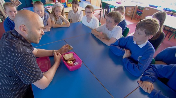 Man shows lunch-box to assorted kids in classroom