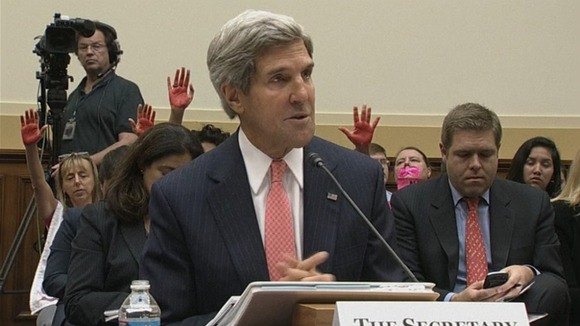 Secretary of State John Kerry seen with the protesters' hands in the background.
