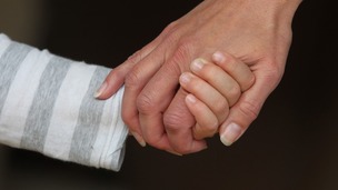 A child and an adult hold hands.