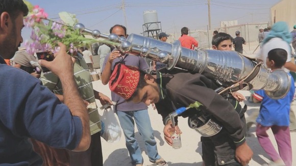 A street vendor pours a cup of coffee from a flask on his back at Zaatari refugee camp in Jordan