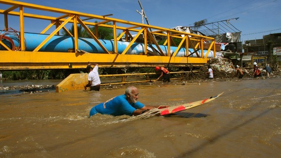 A man uses a surfboard to cross a flooded street in Acapulco.