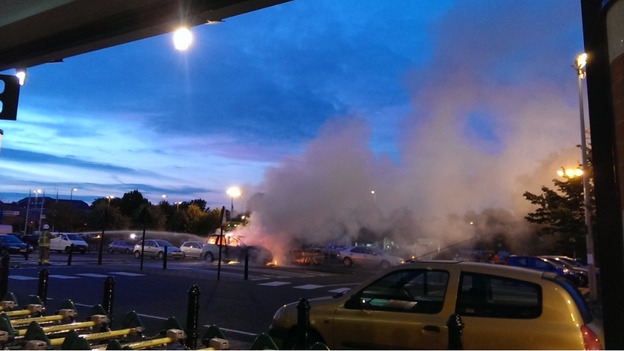 Smoke billows across the car park at a supermarket in Banbury from a car on fire