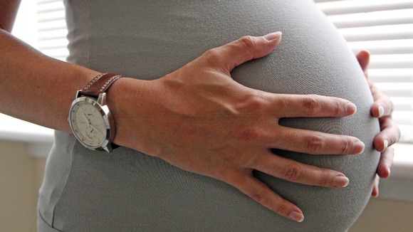 A woman holds her pregnant stomach.