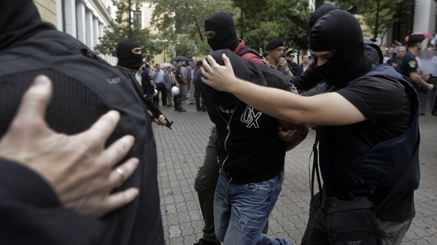 A member of the far-right Golden Dawn party is escorted by anti-terrorism police officers to court in balaclavas.