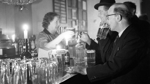 A woman serves beer by candlelight in a pub during a blackout in January 1962.