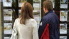 A couple look at properties in the window of an estate agents.
