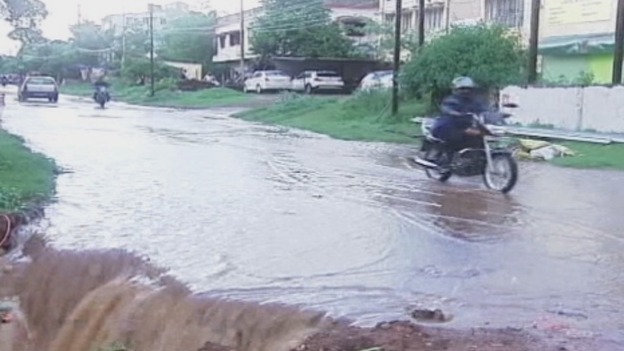 Water cascades off the edge of a road as vehicles drive past